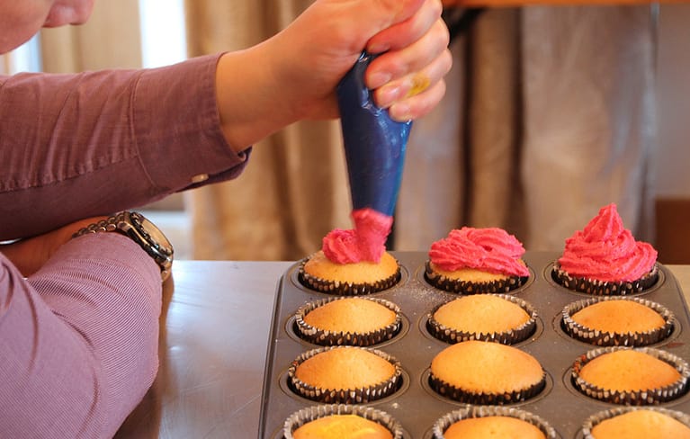 Person icing cupcakes with piping equipment